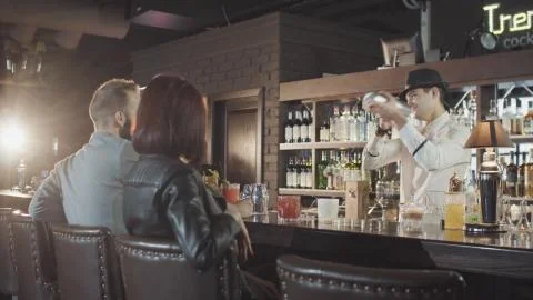 20s bartender is preparing cocktail with shaker behind guests Stock Photos