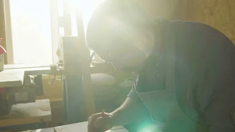20s bearded carpenter woodworker in apron drawing on wooden plank with backlight Stock Footage 76105953