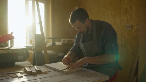 20s bearded man carpenter drawing on wooden board. sunny day in workshop Stock Footage 76106162