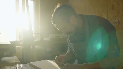 20s bearded man carpenter drawing on wooden board. sunny day in workshop Stock Footage 76106253