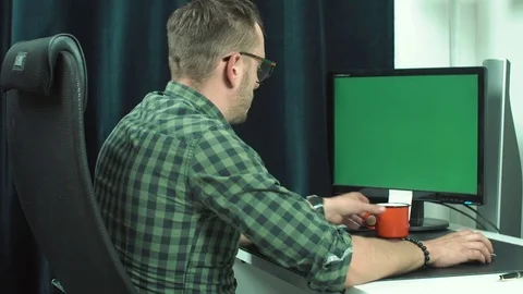 20s man in glasses drinks coffee from a red mug sitting at a table in front of Stock Footage 79676325