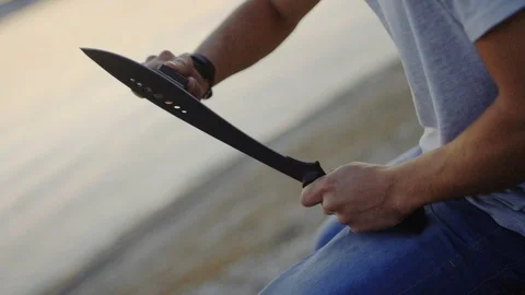 20s man sharpening his machete in the evening sitting on the shore of the bay. Stock Footage 72606439