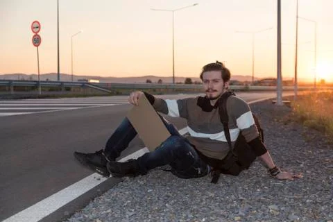 21 years old man sitting on the ground and hitchhiking Stock Photos