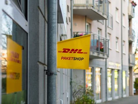 DHL Paketshop (DHL service shop) sign on a building exterior. Service of the Deutsche Post AG to send and receive shipments. Retail store in the city. xkwx brand, building exterior, business, city, commercial, company, courier, delivery, deutsche post ag, dhl paketshop, dresden, europe, facade, flag, germany, logistics, logo, mail, no people, nobody, retail, send and receive, service, shipments, shop, sign, store, symbol, yellow