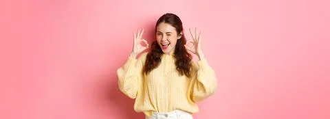 Portrait of cheerful pretty girl winking and saying yes, showing okay sign, alright gesture, praise good job, well done, standing pleased against pink background. xkwx student, girl, background, okay, good, approve, alright, agree, yes, praise, woman, advertising, fashion, beauty, person, portrait, grinning, joy, pink, beautiful, joyful, pleased, positive, smile, stylish, studio, horizontal, young, gesturing, glamour, holiday, excited, shopping, isolated, adult, girlfriend, advertisement, casual, smiling, emotive, slim, upbeat, glamorous, cheerful, emotions, excitement, fashionable, brunette