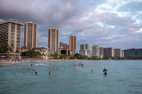 Honolulu,  Hawaii  -  December  29,  2022:  View  of  Waikiki  Beach  with  Diamond  Head  valcano  in  the  distance. xkwx architecture,  beach,  building  exterior,  city  life,  cityscape,  coastline,  diamond  head,  dusk,  famous  place,  hawaii,  hawaii  islands,  honolulu,  hotel,  island,  landscape  scenery,  mountain,  oahu,  ocean,  outdoors,  pacific  islands,  pacific  ocean,  panorama,  panoramic,  relaxation,  royal  hawaiian  hotel,  sand,  sea,  sky,  tourism,  tourist,  travel,  travel  destinations,  trees,  tropical,  tropical  climate,  twilight,  urban  skyline,  usa,  vacation,  waikiki,  waikiki  beach