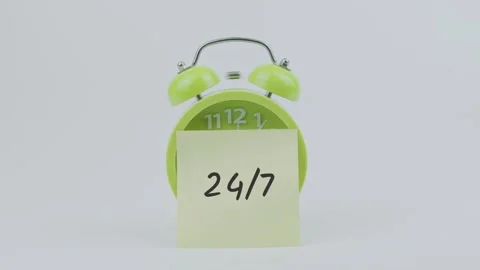 24 7 word on sticky note in front of green clock and ringing on white Stock Footage 313973752