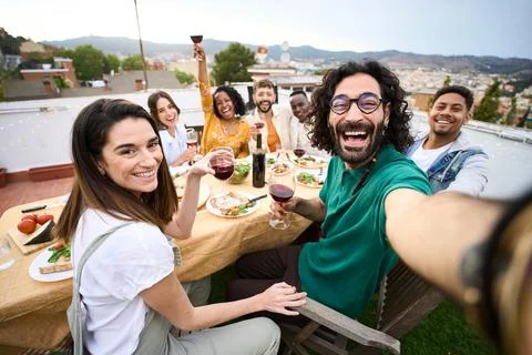 Group of multiracial friends having fun at rooftop party. Man taking selfie to people at barbecue table. Smiling companions enjoy eating and drinking on outdoor terrace. Relationships and celebrations xkwx {rooftop selfie friends happy barbecue group multiracial together party outdoors drinking diverse family people meeting food tasting eating cheerful youth alcohol barbeque bbq beverage birthday brunch celebration hangout home lifestyle lunch picnic vacation having fun taking dinner friendship time smiling terrace positive relations millennial anniversary man women beard}
