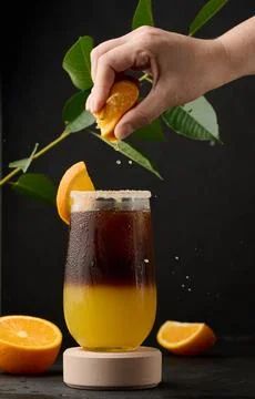 Iced coffee with orange juice in a transparent glass, a woman's hand squeezes an orange slice into a bubble drink xkwx layer coffee orange brown sweet cool ice espresso cold drink glass fresh juice beverage cocktail morning caffeine fruit syrup table yellow citrus juicy bumble slice nobody black hand drop squeeze