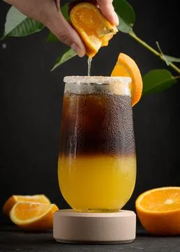 Iced coffee with orange juice in a transparent glass, a woman's hand squeezes an orange slice into a bubble drink xkwx coffee ice juice juicy layer morning nobody orange slice squeeze sweet syrup table yellow cold cool drink drop espresso fresh fruit glass hand beverage black brown bumble caffeine citrus cocktail