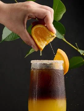 Iced coffee with orange juice in a transparent glass, a woman's hand squeezes an orange slice into a bubble drink xkwx orange slice citrus cocktail coffee cold squeeze sweet syrup table yellow beverage black brown bumble caffeine cool drink drop espresso fresh fruit glass hand ice juice juicy layer morning nobody
