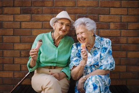 Portrait of two senior female friends in the city, eating ice cream on a hot summer day. Elderly ladies on summer vacation in the city. Pensioners on group trip. Concept of senior vacation and travel groups, clubs. xkwx senior city ice cream woman retirement pensioner lifestyle active outdoor elderly old joy vitality happiness smiling eating street togetherness trendy happy holding tourist cone community bonding enjoyment lady older brick wall sitting travel group travel club senior travel traveling vacation chronic illness diabetes heart disease alzheimers disease mental health osteoporosis arthritis dementia hypertension cholesterol depresion rheumatoid arthritis incontinence