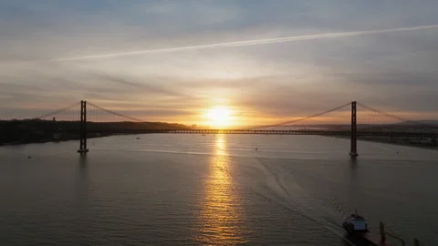 25 de Abril Bridge Glowing at Sunset Above Barge in Lisbon, Portugal Stock Footage 344908868