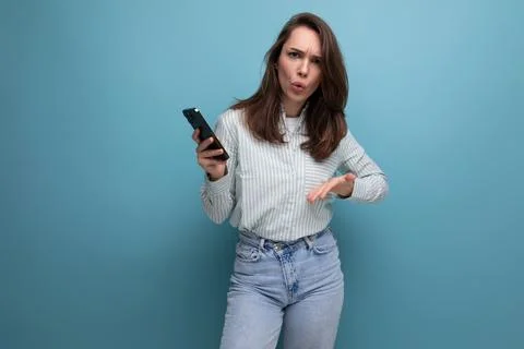 25 year old brunette woman uses a smartphone in her hand on a blue background Stock Photos