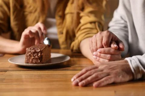 Romantic date. Couple holding hands together at table in cafe, closeup xkwx adult background beautiful bonding boyfriend cafe cake casual closeup couple date dating eat enjoying enjoyment family feelings female flirt focus food girlfriend hands holding indoors lifestyle love lovely lover lovers male man meet meeting people piece relationships restaurant romance romantic selective spending spoon sweetheart table time together togetherness woman wooden