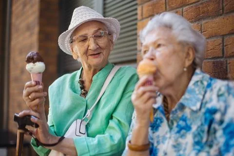 Portrait of two senior female friends in the city, eating ice cream on a hot summer day. Elderly ladies on summer vacation in the city. Pensioners on group trip. Concept of senior vacation and travel groups, clubs. xkwx senior city ice cream woman retirement pensioner lifestyle active outdoor elderly old joy vitality happiness smiling eating street togetherness trendy happy holding tourist cone community bonding enjoyment lady older brick wall sitting travel group travel club senior travel traveling vacation chronic illness diabetes heart disease alzheimers disease mental health osteoporosis arthritis dementia hypertension cholesterol depresion rheumatoid arthritis incontinence