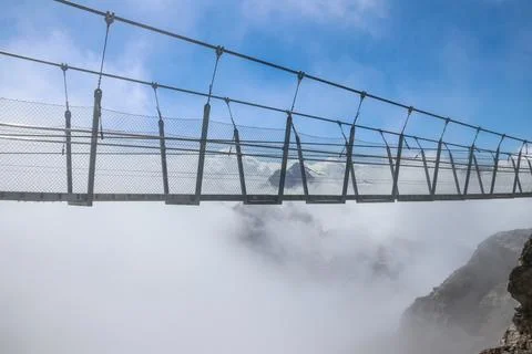 Titlis suspension bridge of steel crossing the peak on top of Titlis glacier in the Uri Alps, Engelberg, Switzerland. Highest suspension bridge in Europe xkwx alpine alps blue bridge cliff cloud destination engelberg europe famous fog footbridge glacier hanging high hiking holiday journey landmark landscape mount mountain nature obwalden outdoor panorama peak rock scenery sightseeing slope snow steel structure summit suspension suspension bridge swiss swiss alps switzerland titlis top tourism travel uri alps vacation view walk white