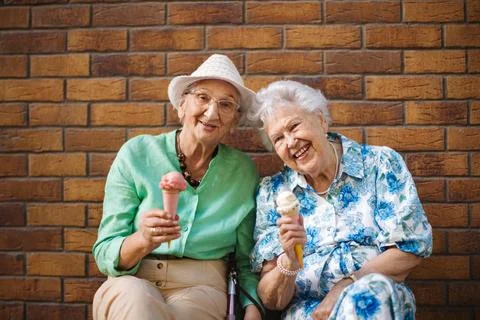 Portrait of two senior female friends in the city, eating ice cream on a hot summer day. Elderly ladies on summer vacation in the city. Pensioners on group trip. Concept of senior vacation and travel groups, clubs. xkwx senior city ice cream woman retirement pensioner lifestyle active outdoor elderly old joy vitality happiness smiling eating street togetherness trendy happy holding tourist cone community bonding enjoyment lady older brick wall sitting travel group travel club senior travel traveling vacation chronic illness diabetes heart disease alzheimers disease mental health osteoporosis arthritis dementia hypertension cholesterol depression rheumatoid arthritis incontinence
