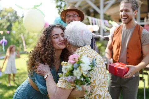 Garden birthday party for senior lady. Beautiful senior birthday woman hugging her granddaughter. xkwx birthday woman senior hugging gifts garden birthday party beautiful woman lady receiving gift granddaughter grandmother embrace smile friends family kiss on cheek celebration joy happiness presents outdoors event festivity gathering special occasion surprise smiles enjoyment togetherness love affection decorations cake memories balloons laughter congratulations wishes entertainment bonding delight cheerful atmosphere friendship gratitude copy space gray hair pearls