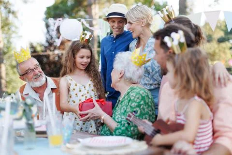Garden birthday party for senior lady. Beautiful senior birthday woman receiving gift from granddaughter, family and friends. Birthday celebration with paper crowns. xkwx birthday woman senior birthday party garden presents gift hugging celeration gifts beautiful woman lady receiving embrace smile friends family grandmother grandson celebration joy happiness outdoors event festivity gathering special occasion surprise smiles enjoyment togetherness love affection decorations cake memories balloons laughter congratulations wishes entertainment bonding delight cheerful atmosphere friendship gratitude copy space gray hair pearls