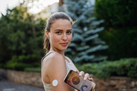 Portrait of woman with diabetes connecting her smartphone to continuous glucose monitor sensor before exercising. Diabetic woman checking her blood sugar levels in real time before running. xkwx diabetic woman preparing exercise outdoor city young running continuous glucose monitor health sensor diabetes management lifestyle urban active medical device training health-conscious endurance technology glucose diabetes sport connecting motivation chronic condition routine mobile app street workout modern health determination resilience challenge medicine therapy adaptation empowerment increase insulin decrease insulin adjust physical activity affecting ketones screen display copy space National Diabetes Month november World Diabetes Day