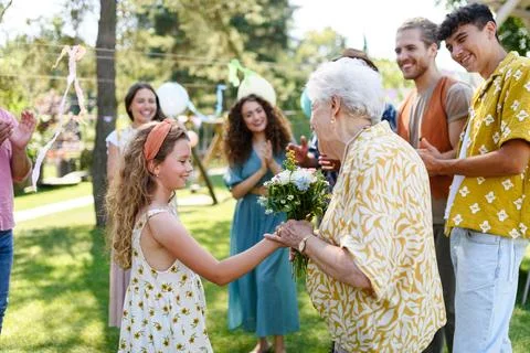 Garden birthday party for senior lady. Beautiful senior birthday woman receiving flowers from granddaughter. xkwx birthday woman senior flowers gifts garden birthday party beautiful woman lady receiving gift bouquet friends family grandmother granddaughter celebration joy happiness presents outdoors event festivity gathering special occasion surprise smiles enjoyment togetherness love affection decorations cake memories balloons laughter congratulations wishes entertainment bonding delight cheerful atmosphere friendship gratitude copy space gray hair pearls