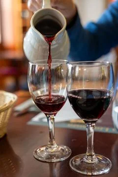 Pouring yound red beaujolais wine in glasses during celebration of end of harvest and first sale release on third Thursday of November from white ceramic pitcher in Limouges, France xkwx Gamay agriculture autumn taste background beaujolais beaujolais nouveau beverage bordeaux bottle burgundy celebration corkscrew drink festival food france french wine fruit glass grape grapes harvest marketing november party pouring red red wine red wine bottle red wine glass release restaurant tanin tasting third thursday traditional vine vineyard vintage violet wineglass winery young