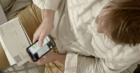 28Man pays invoice with qr code via internet banking. He is sitting on the couch 스톡 동영상 201166339