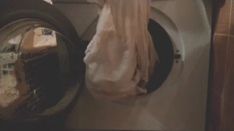 A 29-year-old man pulls clean white bedding out of the washing machine Stock Footage 157280241