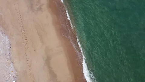 2K Drone top down shot moving slowly over sea waves with footprints on the sand. 動画素材 336864560