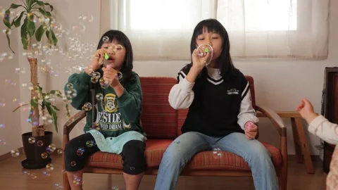 3 asian sisters playing with soap bubble at home. Baby tries to catch bubbles. Stock Footage 228276967