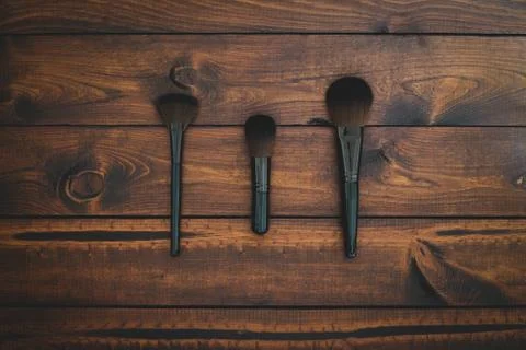 3 assorted makeup brushes on a brown rustic wood background Stock Photos