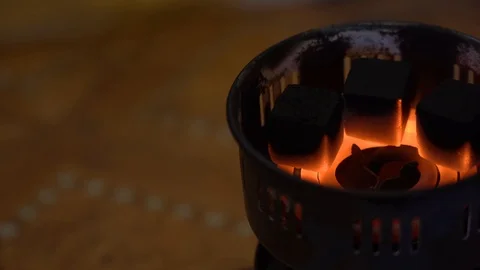 3 black square coals cook and blush on a red-hot spiral on a blurry background. Video stock 125456318