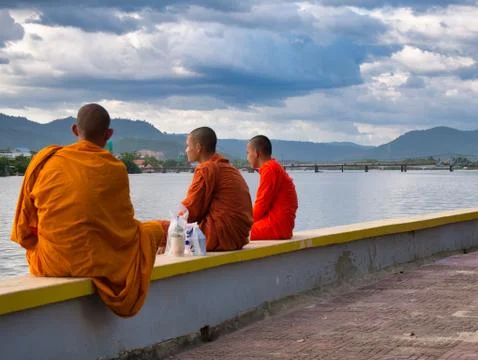 3 Buddhist monks sit next to the Preaek Tuek Chhu River at Kampot, Cambodia Stock Photos