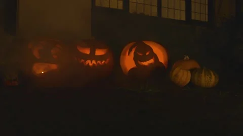 3 carved lit pumpkins outside the front of a house halloween with smoke and  Stock Footage 137327924