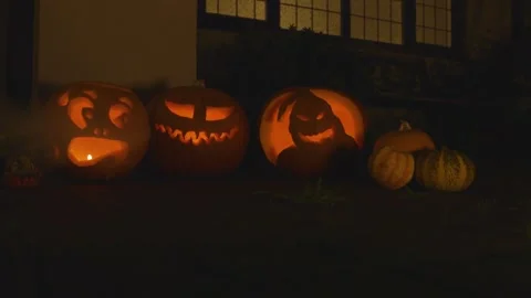 3 carved lit pumpkins outside the front of a house Halloween with smoke Stock Footage 137781048