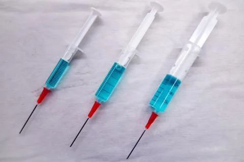 3 differently sized syringes filled with blue liquid lie on a white compress Stock Photos