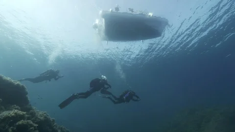 3 divers swim under their boat, Ustica, Mediterranean sea Stock Footage 124497834