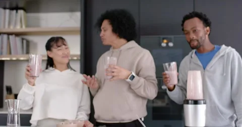3 friends standing at kitchen island, ring light starting film, blender running Stock Footage 345590189