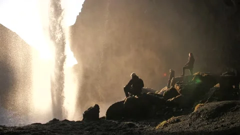 3 men sitting behind a waterfall in iceland with sunset Stock Footage 158746629
