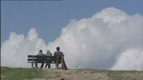 3 people sit on bench on top of dike watching white cloud in Dutch blue sky Stock Footage 570367