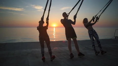 3 persons doing exercises with trx at sunrise. Slow motion. Stock Footage 67986572