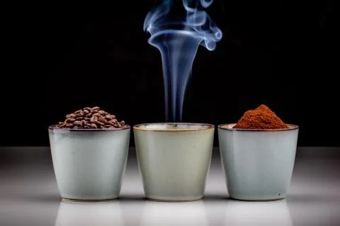 3 rustic coffee cups with coffee grounds, smoking coffee, and ground coffee. Foto stock
