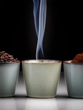 3 rustic coffee cups with coffee grounds, smoking coffee, and ground coffee. Stock Photos