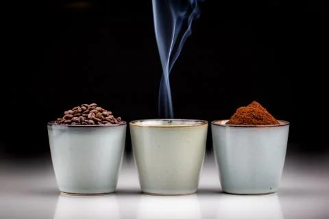 3 rustic coffee cups with coffee grounds, smoking coffee, and ground coffee. Stock Photos