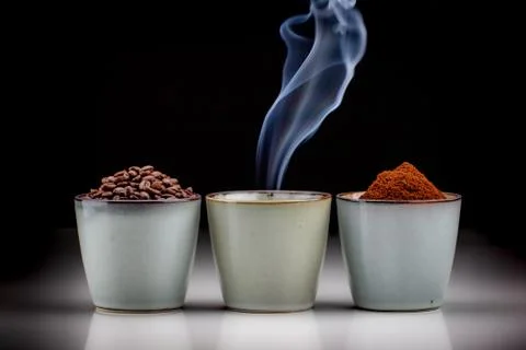 3 rustic coffee cups with coffee grounds, smoking coffee, and ground coffee. Stock Photos