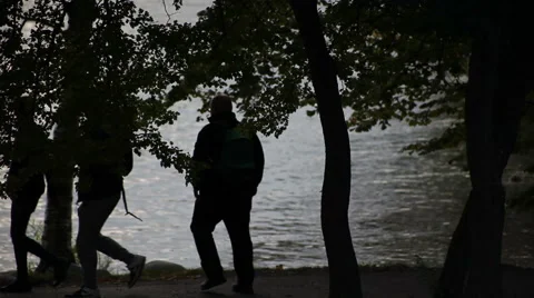 3 Silhouetted men walking by the river near trees. A bicycle passing too. Stock Footage 44057492