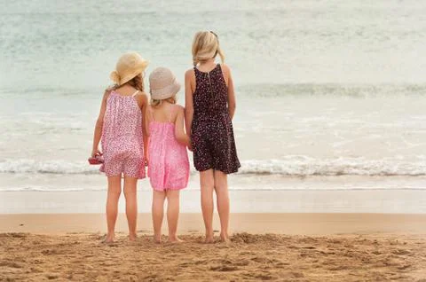 3 sisters stand on beachfront facing the ocean. Stock Photos