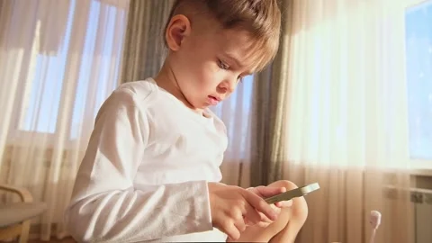 3 three old kid using gadget mobile smartphone while sitting on the chair Stock Footage 231108424