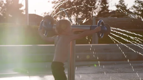 3 year old boy spins large splash pad water feature with two spraying nozzles Stock Footage 233940992